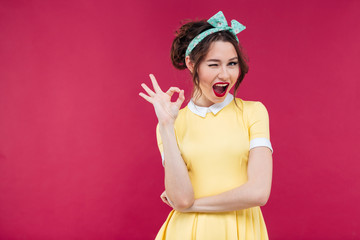 Happy attractive pinup girl in yellow dress showing ok sign