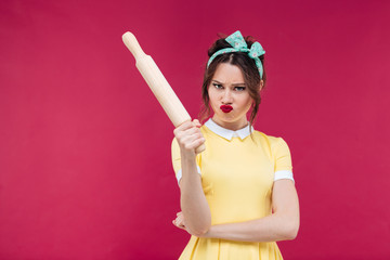 Mad irritated young woman in yellow dress with rolling pin