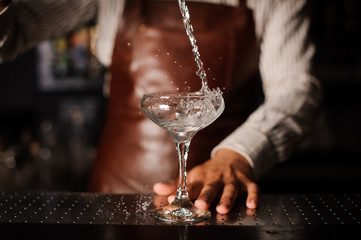 Barman pouring into champagne glass and making a splash