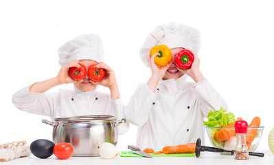 two little cooks in uniform playing vegetables for soup in the kitchen
