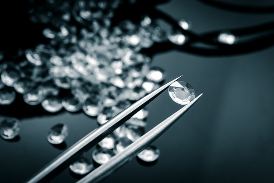 Monochrome image of a jeweler inspecting with tweezers one diamond of the many diamonds in a pile that spilled from a bag