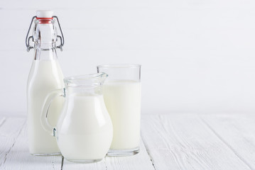 Milk bottle with jug and glass of milk on vintage white wooden table