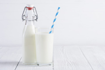 Glass of milk with paper straw and milk bottle on wooden white table still life