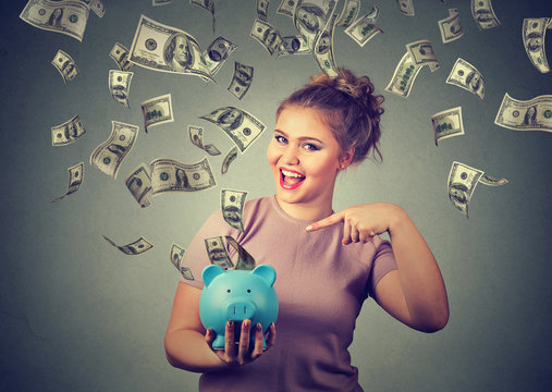 happy woman with piggy bank celebrates success under money rain falling down dollar bills