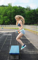 The beautiful sportswoman jumps on a bench up.