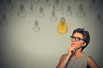 Portrait thinking woman in glasses looking up with light idea bulb above head