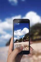 Taking picture of beach scene with smart phone. Blurred background. Can see sky, clouds, water and...