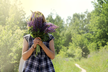 floral hide and seek outdoors/ girl in a plaid summer dress hiding her face behind a bouquet of wild flowers 