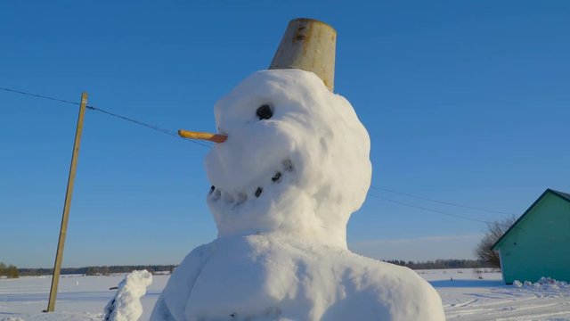 A small pail on the snowmans head. The big snowman has a carrot nose with a pail on his head