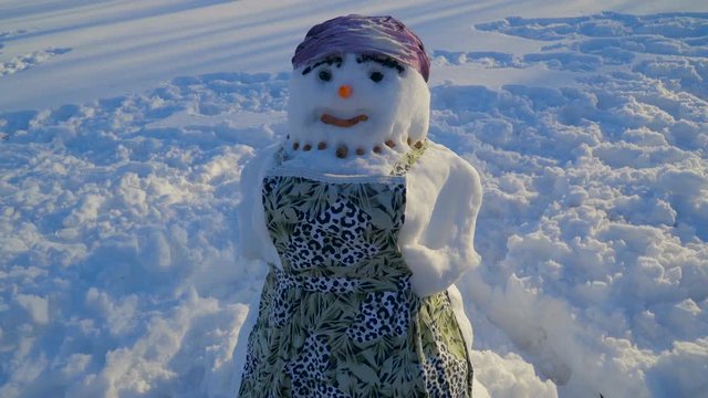 A snowman with an apron on his body. It is a color striped green apron around his body and a headdress on the top