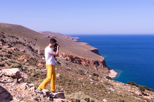 man taking a picture of the landscape against the sea 