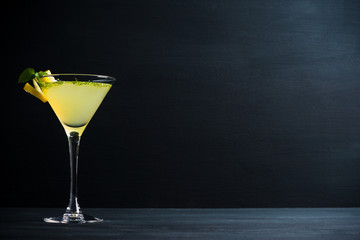 Gelber Martini-Cocktail mit Zitrone und Minze auf rustikalem Holzhintergrund