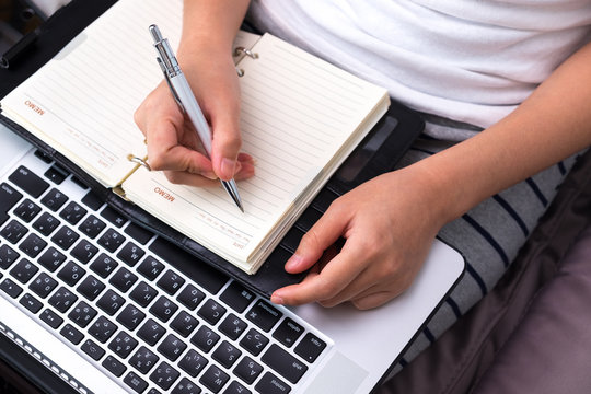 female hands with pen writing on notebook with laptop.