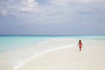 Fototapeta na wymiar Young girl walking on an empty white sand beach, back view