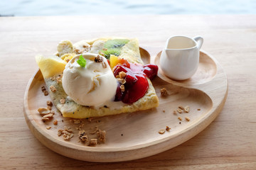 Melting vanilla ice cream on mixed fruit crepe with honey pot in wooden plate, there is a blank space for placing logos on wooden plate. Outdoor shot.