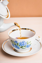 Old-style porcelain kettle pouring tea from jug to cup of tea