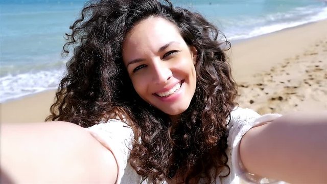 Portrait of pretty young woman taking selfie with a smart phone on the beach, slow motion