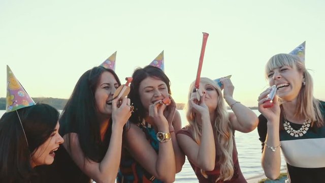 A friendly group of girls celebrating on the beach. Holiday horns and hats involved. Slow motion.