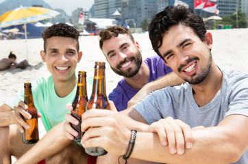 Lachender Latino trinkt mit Freunden Bier am Strand