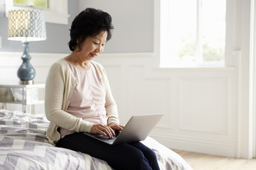 Fototapeta premium Senior Woman Sitting On Bed Using Laptop Computer