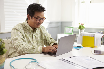 Fototapeta premium Male Doctor Sitting At Desk Working At Laptop In Office