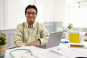 Fototapeta premium Male Doctor Sitting At Desk Working At Laptop In Office