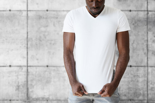 T-shirt design and advertising concept. Cropped studio portrait of dark skinned young male posing against white copy space wall wearing white T-shirt with copy space for your advertising content