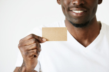 Cropped shot of African male hands holding blank card with copy space for your text or advertising content. Successful smiling businessman wearing white T-shirt showing business card. Film effect