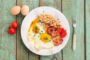 Homemade breakfast of fried eggs, bacon, beans and tomatoes on w