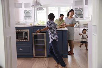 Parents Prepare Food As Children Play In Kitchen - Powered by Adobe