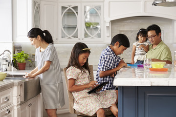 Family In Kitchen Doing Chores And Using Digital Devices