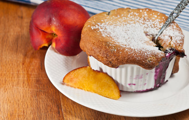 Blueberry Peach Cobbler in a ceramic cup on a white plate with sliced peach and a spoon