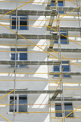 scaffolding near a house under construction for external plaster works, high apartment building in city, white wall and window, yellow pipe