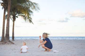 Portrait of young mother with her adorable little boy on the ocean beach. Happy woman with toddler enjoying vacation by the sea. On the empty beach. Motherhood.
