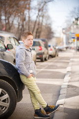 Portrait of handsome school kid boy standing near the car and looking into distance. outdoors. Teen child on the street.