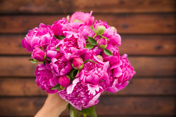 Beautiful bouquet of dark pink peonies in woman hands on a wooden background. Bunch of flowers in hands. Stripes. Summer time.
