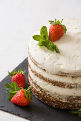 Delicious white cream icing cake with strawberry on the black board. Naked cake with cream, decorated with strawberries and mint.
