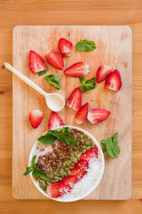 Breakfast berry smoothie bowl topped with strawberry, pumpkin seeds, coconut, muesli and fresh mint. Strawberry banana smoothie bowl. healthy breakfast or snack, wooden tableware.