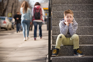 Child sitting on the stone steps. Portrait of handsome kid boy wearing casual sitting on the stairs on the street. Stylish boy looking at camera. Teenage boy, child outdoors in summer or spring.