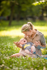 Beautiful young mother with adorable baby boy relaxing sitting on grass on background summer meadow. Summer outdoor portrait of happiness. mother with child in the park on the wild flowers meadow.