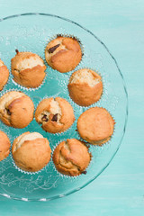 Delicious homemade vanilla muffins with chocolate on the glass plate on turquoise background. Sweet dessert for celebration, party or snack. Cupcakes.