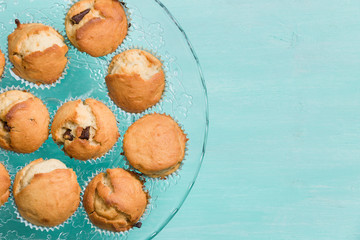 Delicious homemade vanilla muffins with chocolate on the glass plate on turquoise background. Sweet dessert for celebration, party or snack. Cupcakes.