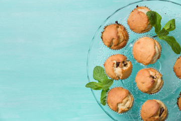 Delicious homemade vanilla muffins with chocolate and mint on the glass plate on turquoise background. Sweet dessert for celebration, party or snack. Cupcakes.