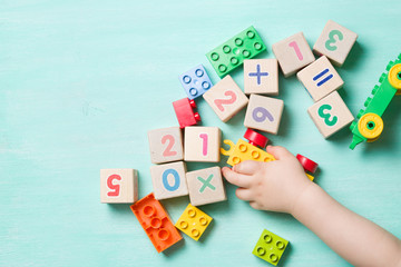 Child playing with wooden cubes with numbers and colorful toy bricks on a turquoise wooden...