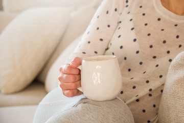Girl with coffee mug sitting on the sofa indoors. Woman drinking a cup of  coffee or tea sitting cozy at home. Relax and rest.
