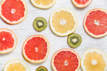 Top view on cut red and yellow grapefruit and kiwi on white wooden background. Juicy and fresh fruit. Healthy eating concept. Flat lay.
