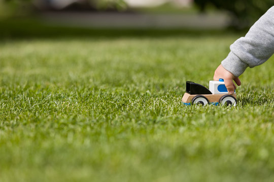 Closeup of child's hand playing with toy cay on the green grass in the park. Toddler boy playing with small car. Daycare and nursery. Outdoors. Childhood and lifestyle concept. Activities for children