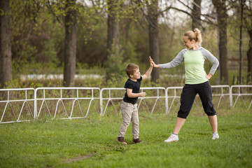 Obraz premium Happy son and mother are doing exercises in the summer park. on the stadium, outdoor. Sport activities with children. Healthy lifestyle. Fitness exercises. Young mother and son are stretching together