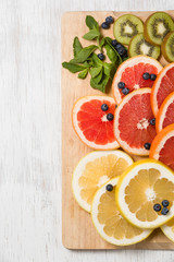 Top view on cut red and yellow grapefruit with mint. Fresh organic citrus, kiwi and blueberry on white wooden background. Healthy snack or fruit dessert.