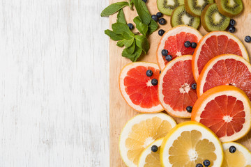 Top view on cut red and yellow grapefruit with mint. Fresh organic citrus, kiwi and blueberry on white wooden background. Healthy snack or fruit dessert.
